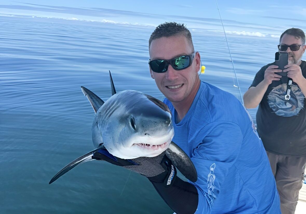 Man holding small shark on a boat.